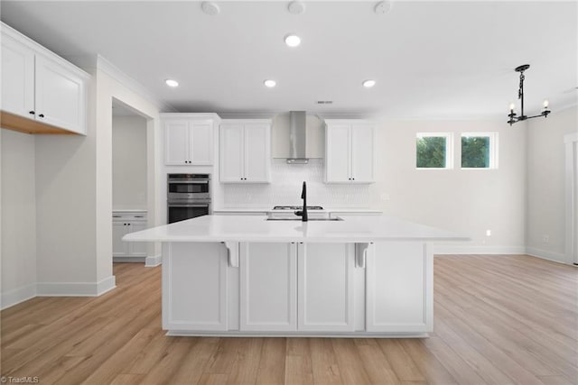 kitchen with baseboards, light countertops, double oven, and wall chimney range hood
