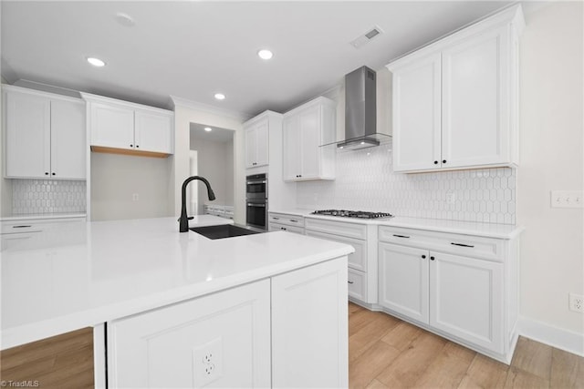 kitchen featuring wall chimney range hood, a sink, stainless steel double oven, white cabinetry, and visible vents