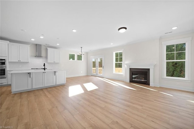 unfurnished living room with a sink, a glass covered fireplace, light wood finished floors, baseboards, and recessed lighting
