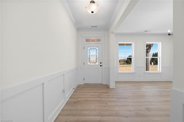 foyer entrance with wainscoting, crown molding, and light wood-style floors