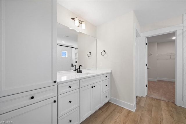 bathroom featuring baseboards, wood finished floors, a spacious closet, and vanity