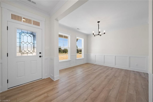 foyer entrance featuring crown molding, wainscoting, a chandelier, light wood-style flooring, and visible vents