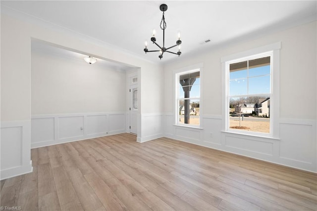 unfurnished dining area with light wood-type flooring, visible vents, a wainscoted wall, and a notable chandelier