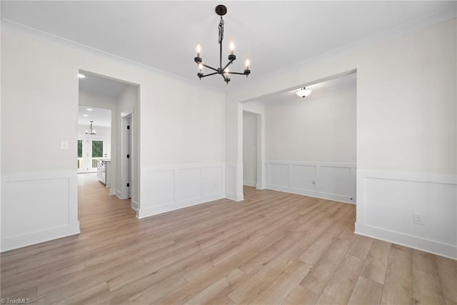 unfurnished dining area with a decorative wall, a notable chandelier, a wainscoted wall, and light wood-type flooring