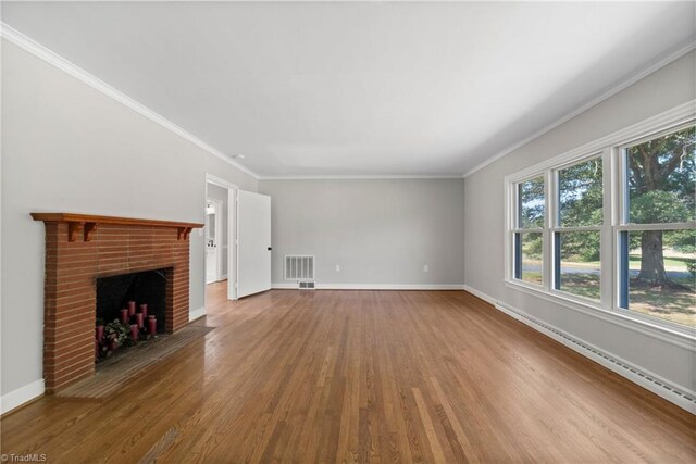 unfurnished living room with baseboard heating, wood-type flooring, ornamental molding, and a brick fireplace