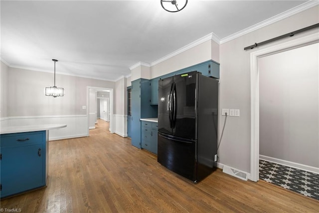 kitchen with crown molding, blue cabinetry, dark hardwood / wood-style floors, black fridge, and pendant lighting