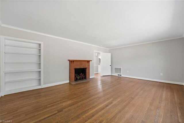 unfurnished living room with built in features, ornamental molding, hardwood / wood-style floors, and a brick fireplace