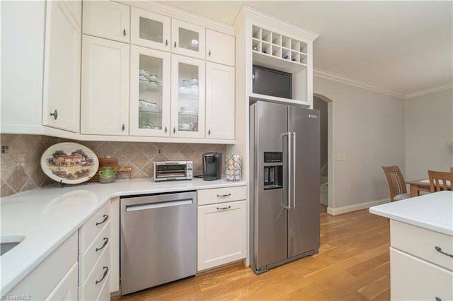 kitchen with crown molding, light wood-style floors, arched walkways, light countertops, and appliances with stainless steel finishes