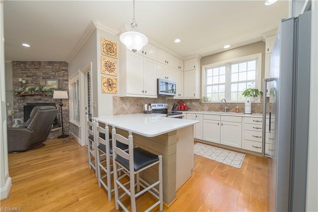 kitchen featuring light wood-type flooring, decorative backsplash, a peninsula, appliances with stainless steel finishes, and white cabinetry