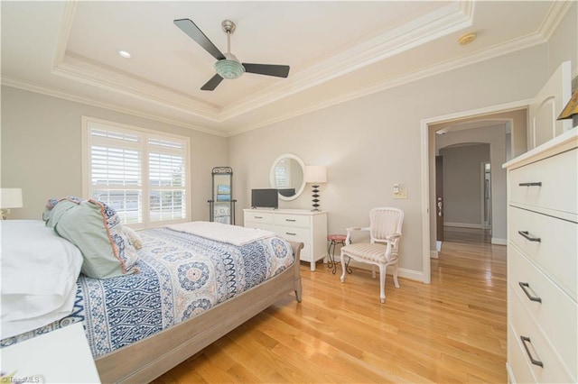 bedroom featuring a ceiling fan, light wood-style floors, arched walkways, a tray ceiling, and ornamental molding
