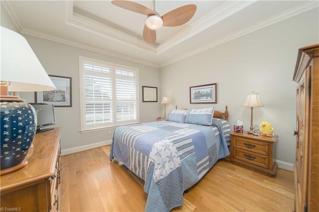 bedroom with crown molding, ceiling fan, a tray ceiling, light wood finished floors, and baseboards