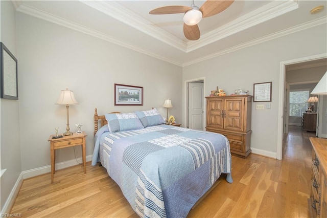 bedroom featuring light wood finished floors, baseboards, a tray ceiling, and crown molding