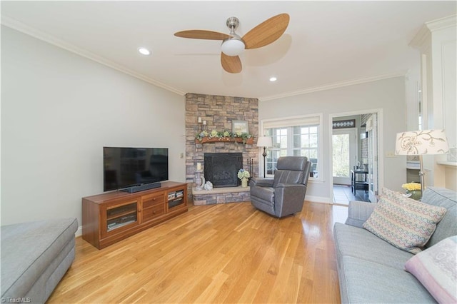 living room with recessed lighting, a stone fireplace, a ceiling fan, ornamental molding, and light wood-style floors