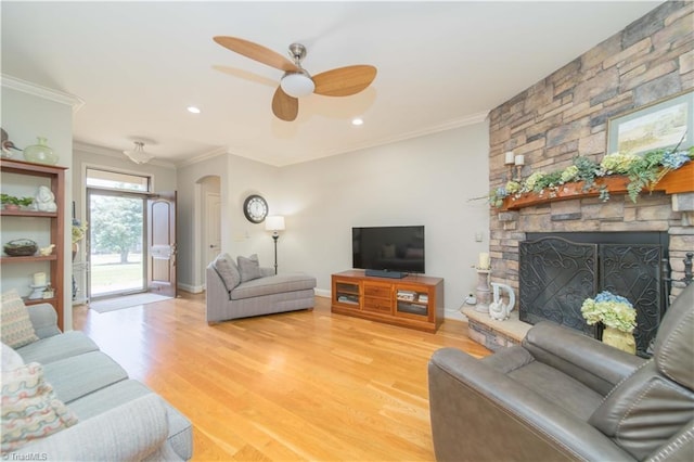living area featuring ceiling fan, ornamental molding, a stone fireplace, and light wood finished floors