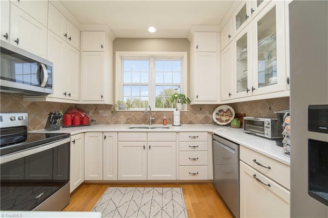 kitchen featuring tasteful backsplash, a sink, stainless steel appliances, light wood finished floors, and light countertops