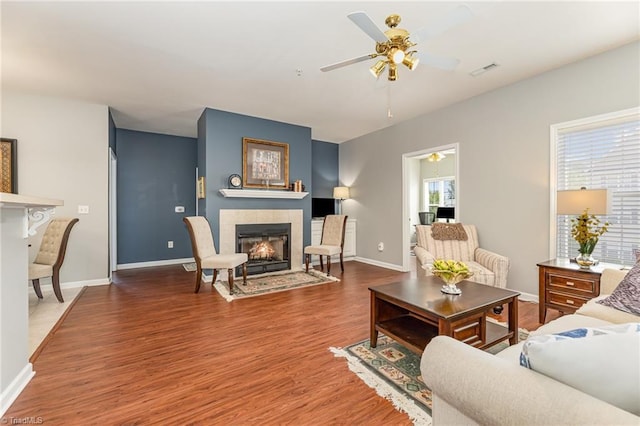 living room featuring visible vents, wood finished floors, baseboards, ceiling fan, and a tiled fireplace