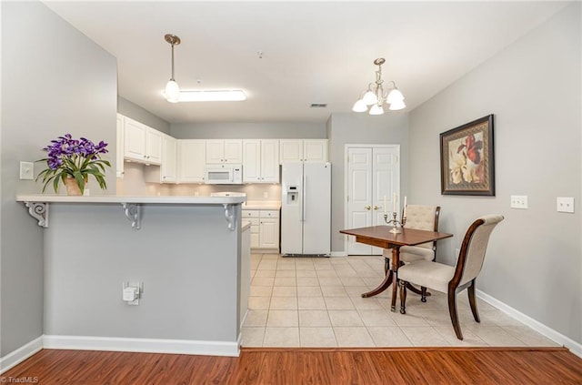 kitchen featuring white appliances, light countertops, a chandelier, a peninsula, and a kitchen bar