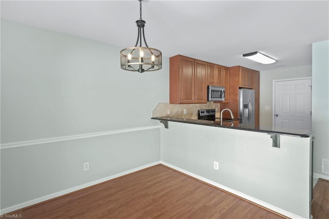 kitchen featuring wood finished floors, a breakfast bar, a peninsula, stainless steel appliances, and dark countertops