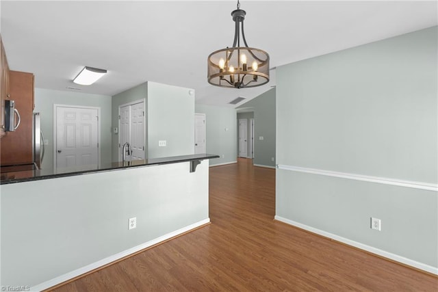 kitchen with baseboards, an inviting chandelier, a peninsula, dark wood-type flooring, and dark countertops