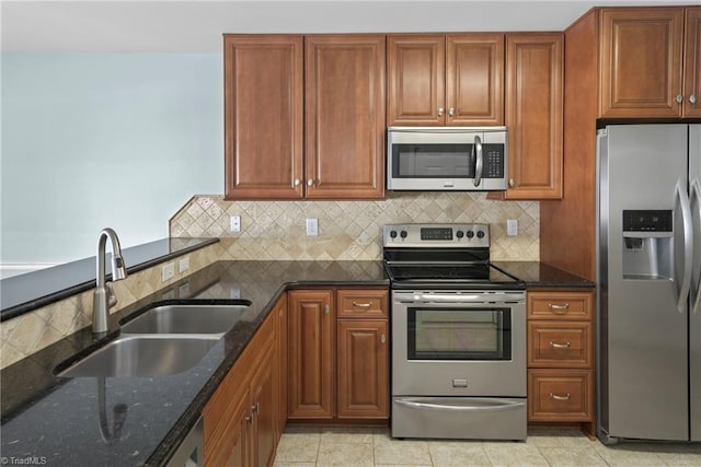 kitchen featuring tasteful backsplash, dark stone countertops, appliances with stainless steel finishes, light tile patterned flooring, and a sink