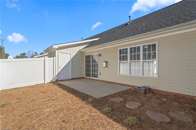 rear view of house with roof with shingles, a patio, and fence