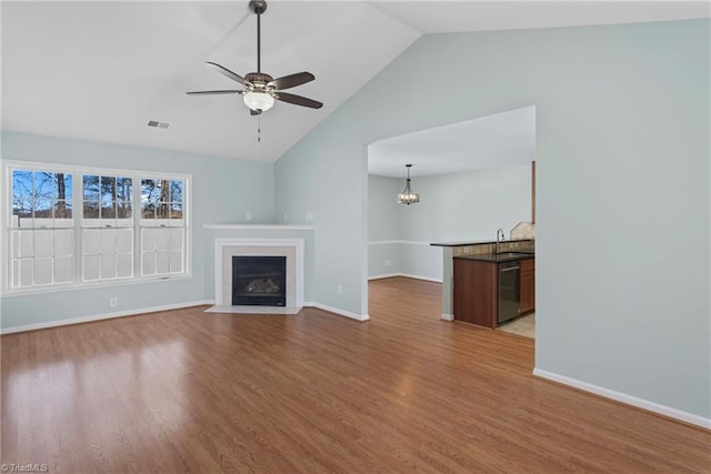 unfurnished living room with wood finished floors, visible vents, a fireplace with flush hearth, a sink, and ceiling fan with notable chandelier