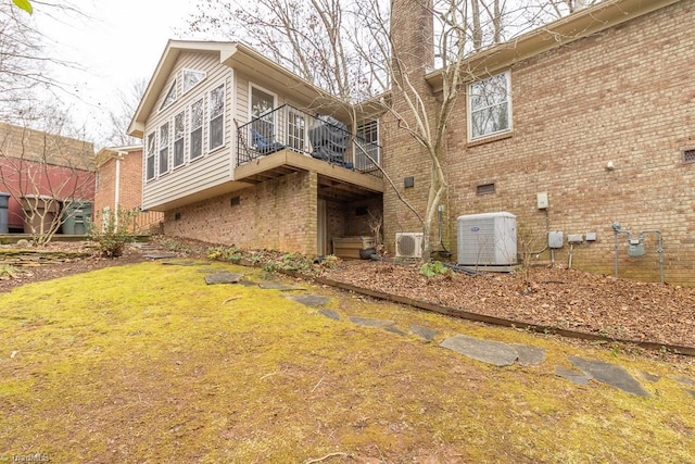 rear view of house featuring central AC unit, a balcony, and a yard