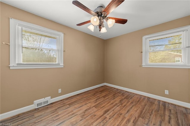 spare room featuring a healthy amount of sunlight, baseboards, visible vents, and wood finished floors