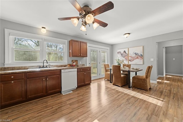 kitchen featuring light wood-style flooring, a sink, a ceiling fan, baseboards, and dishwasher