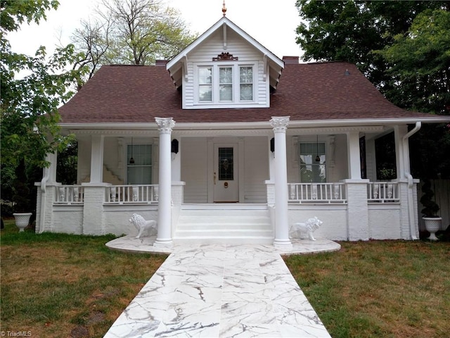 view of front of home with covered porch, a shingled roof, and a front yard