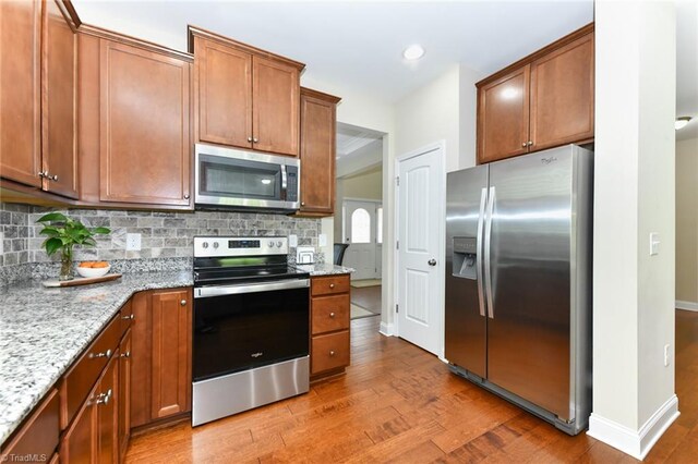 kitchen featuring light wood-type flooring, decorative backsplash, stainless steel appliances, and light stone counters