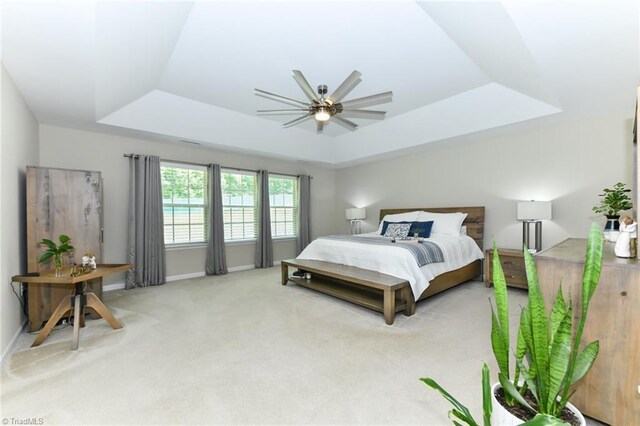 bedroom featuring a tray ceiling, light carpet, and ceiling fan