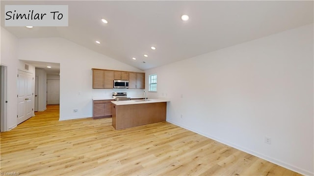 kitchen with vaulted ceiling, appliances with stainless steel finishes, kitchen peninsula, sink, and light hardwood / wood-style flooring