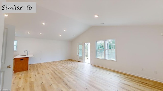 unfurnished living room with sink, light wood-type flooring, and vaulted ceiling