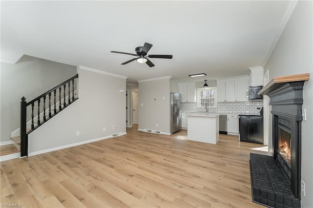 kitchen featuring a center island, crown molding, stainless steel appliances, a glass covered fireplace, and open floor plan