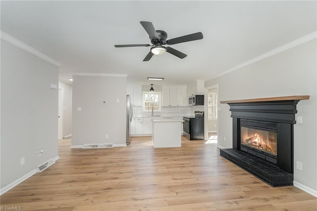 unfurnished living room with visible vents, ornamental molding, a glass covered fireplace, light wood-type flooring, and baseboards