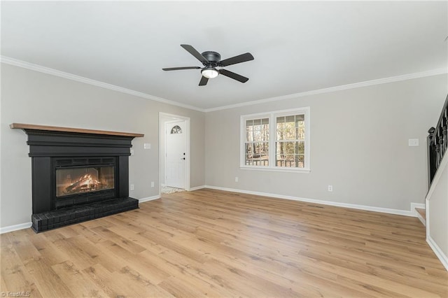 unfurnished living room with ornamental molding, light wood finished floors, a glass covered fireplace, and baseboards