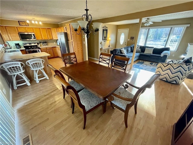 dining space featuring sink, ceiling fan with notable chandelier, a textured ceiling, and light wood-type flooring