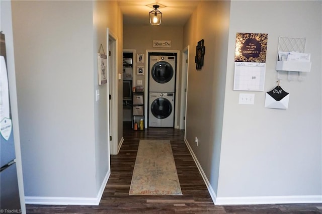 clothes washing area with stacked washer / dryer, dark wood finished floors, and baseboards
