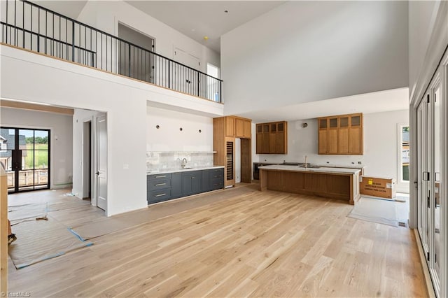 1341 Maple Chase Ln, Winston-Salem, NC 27106 - kitchen featuring a towering ceiling, light wood-type flooring, brown cabinetry, a center island with sink, and light countertops