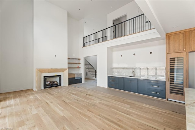 1341 Maple Chase Ln, Winston-Salem, NC 27106 - unfurnished living room featuring wine cooler, bar with sink, stairs, light wood-style floors, and a towering ceiling