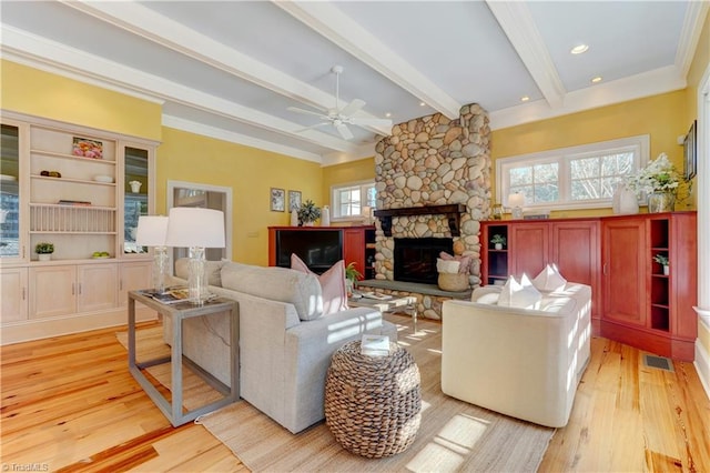 living room featuring beamed ceiling, ceiling fan, a stone fireplace, and light hardwood / wood-style flooring