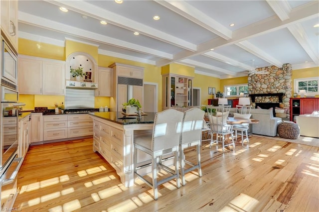 kitchen featuring a kitchen bar, built in appliances, beamed ceiling, a fireplace, and a kitchen island with sink