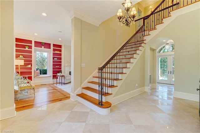 stairway with an inviting chandelier, built in shelves, a wealth of natural light, and french doors