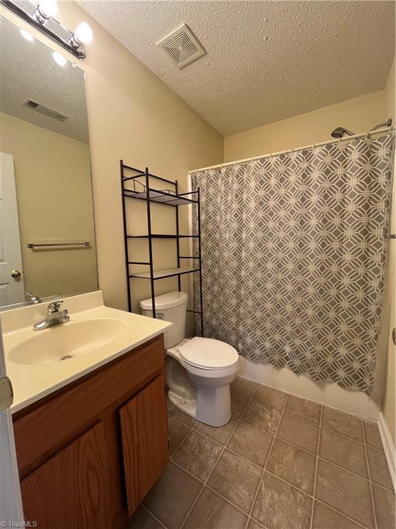 full bathroom with shower / tub combo with curtain, vanity, a textured ceiling, tile patterned floors, and toilet