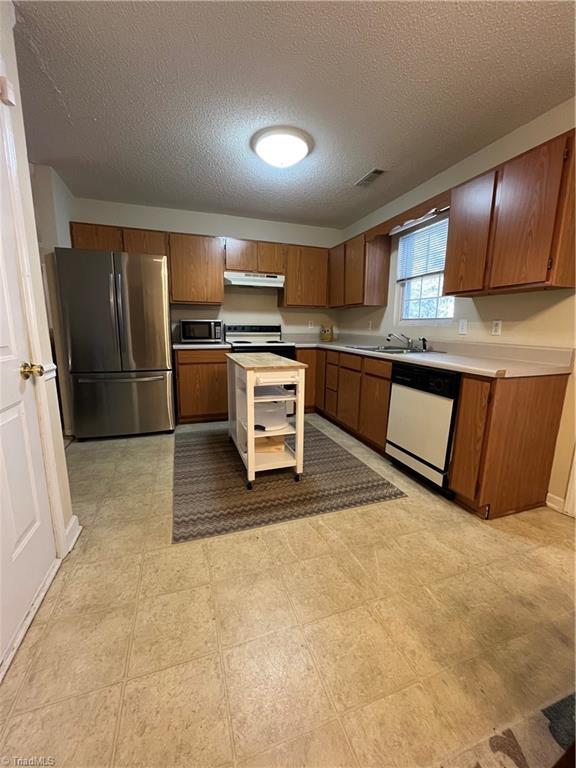 kitchen with stainless steel refrigerator, dishwasher, sink, a textured ceiling, and electric stove