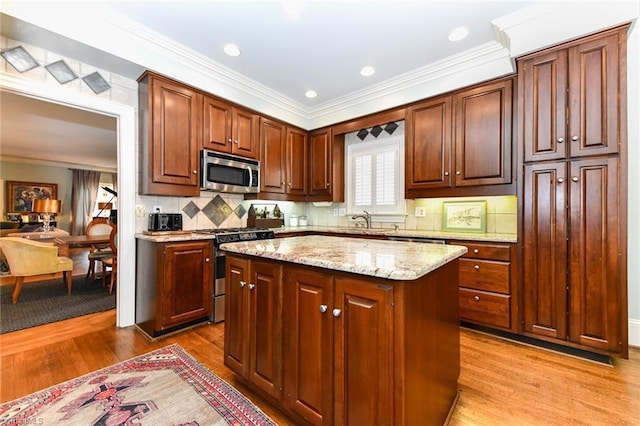 kitchen featuring a kitchen island, ornamental molding, appliances with stainless steel finishes, wood finished floors, and a sink