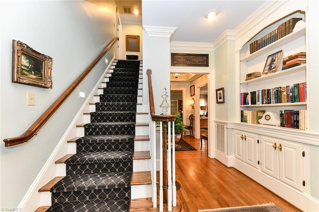 stairs featuring crown molding, built in features, wood finished floors, and visible vents