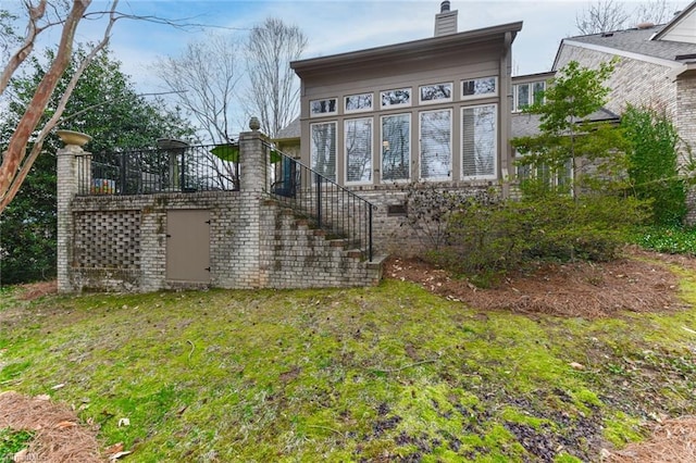 back of house with stairs, a yard, and a chimney