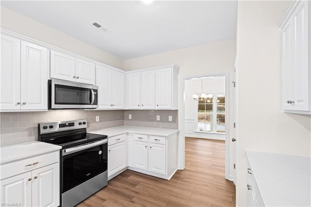 kitchen with visible vents, light wood finished floors, stainless steel appliances, decorative backsplash, and light countertops